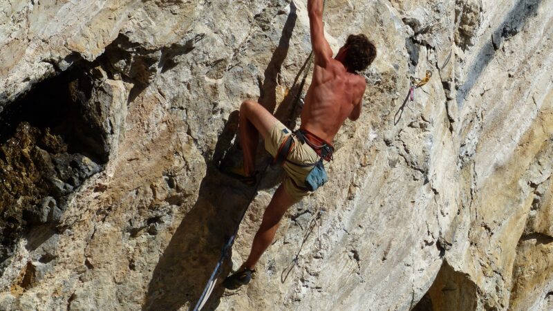Ein Mann klettert an einer sonnenbeschienenen Felswand hoch.