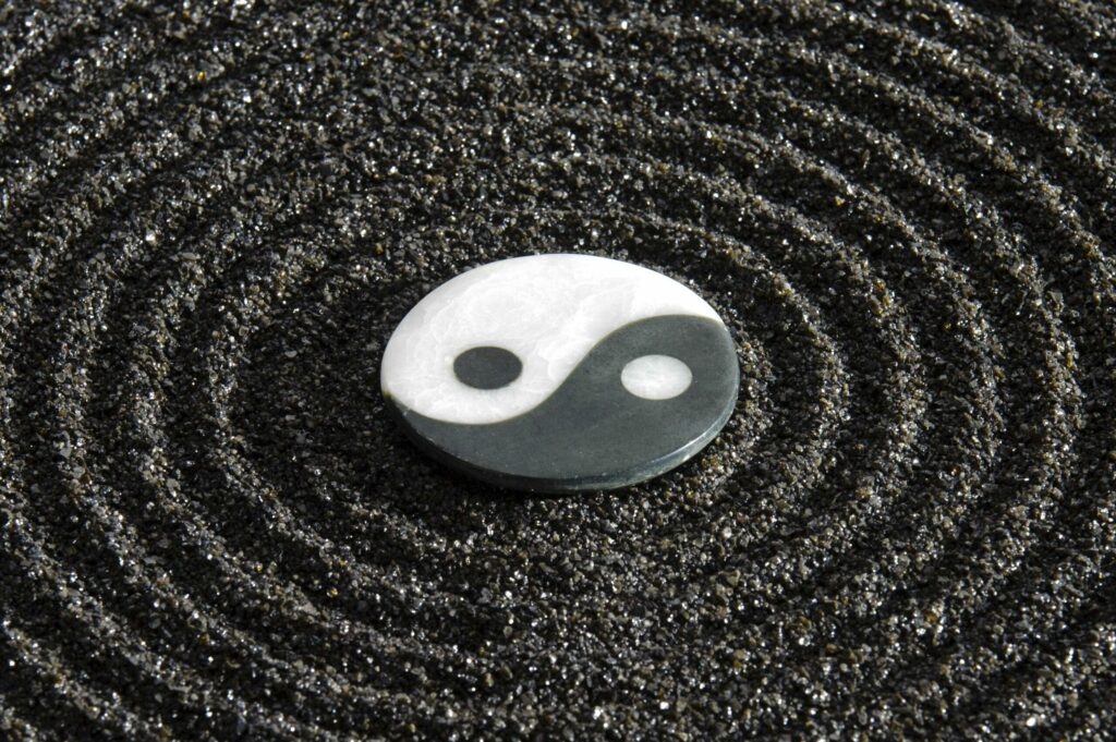 Liegendes Yin-Yang-Symbol aus Stein. Die obere Hälfte ist weiß, die untere schwarz, mit einem kleinen Punkt der jeweils anderen Farbe in jeder Hälfte.