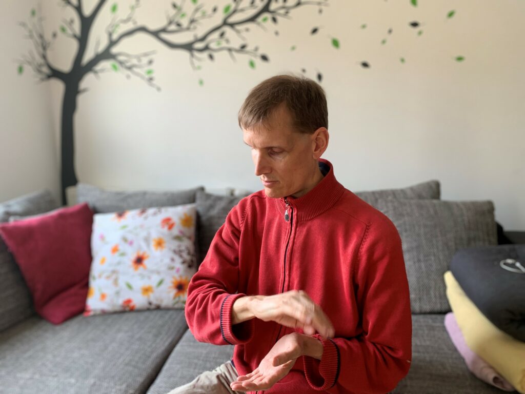 Clemens Pistauer sitzt auf einem Sofa und arbeitet energetisch. Er trägt eine rote Weste. Für die Energiearbeit hält er seine Hände vor seinem Oberkörper.