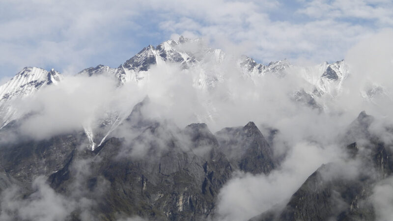 Gipfelpanorama im Himalaya. Die höheren Gipfel sind teilweise mit Schnee bedeckt und von Wolken verhüllt.