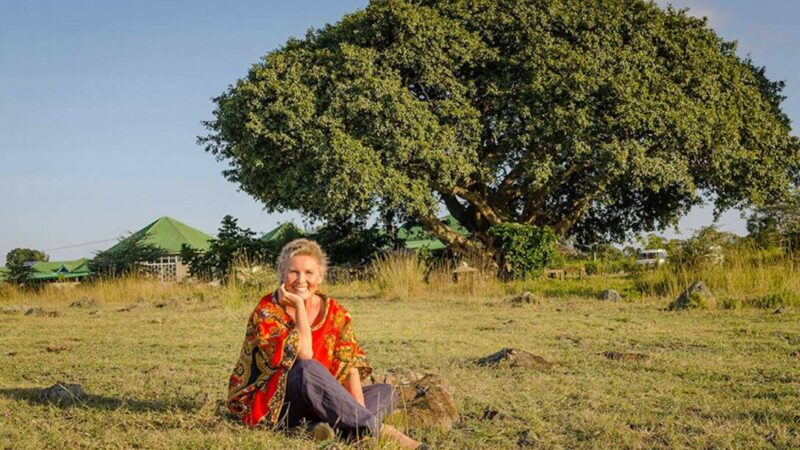 Dr. Christine Wallner sitzt vor einem sehr großen Baum in Momella, Tansania.