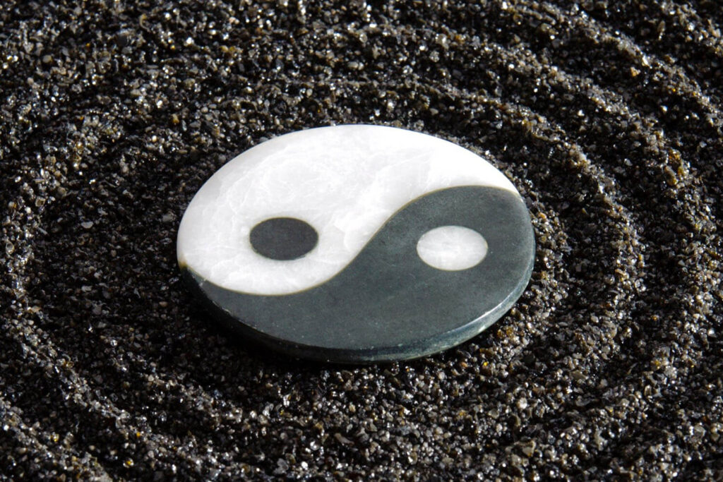 Auf dunklem Untergrund liegt eine kreisrunde, flache Steinscheibe, die das Yin-Yang-Symbol darstellt.