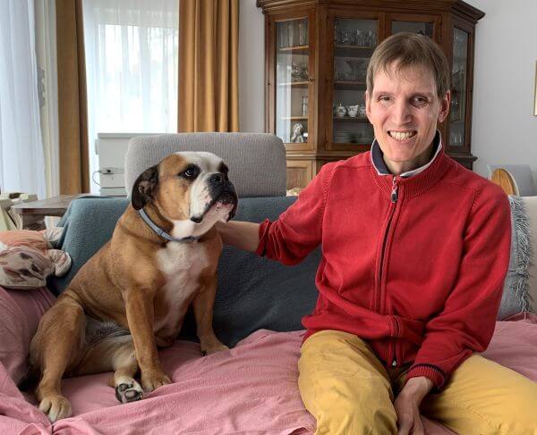 Clemens Pistauer sitzt neben einer Bulldogge, die er energetisch behandelt hat. Seine rechte Hand liegt auf ihrer Schulter.